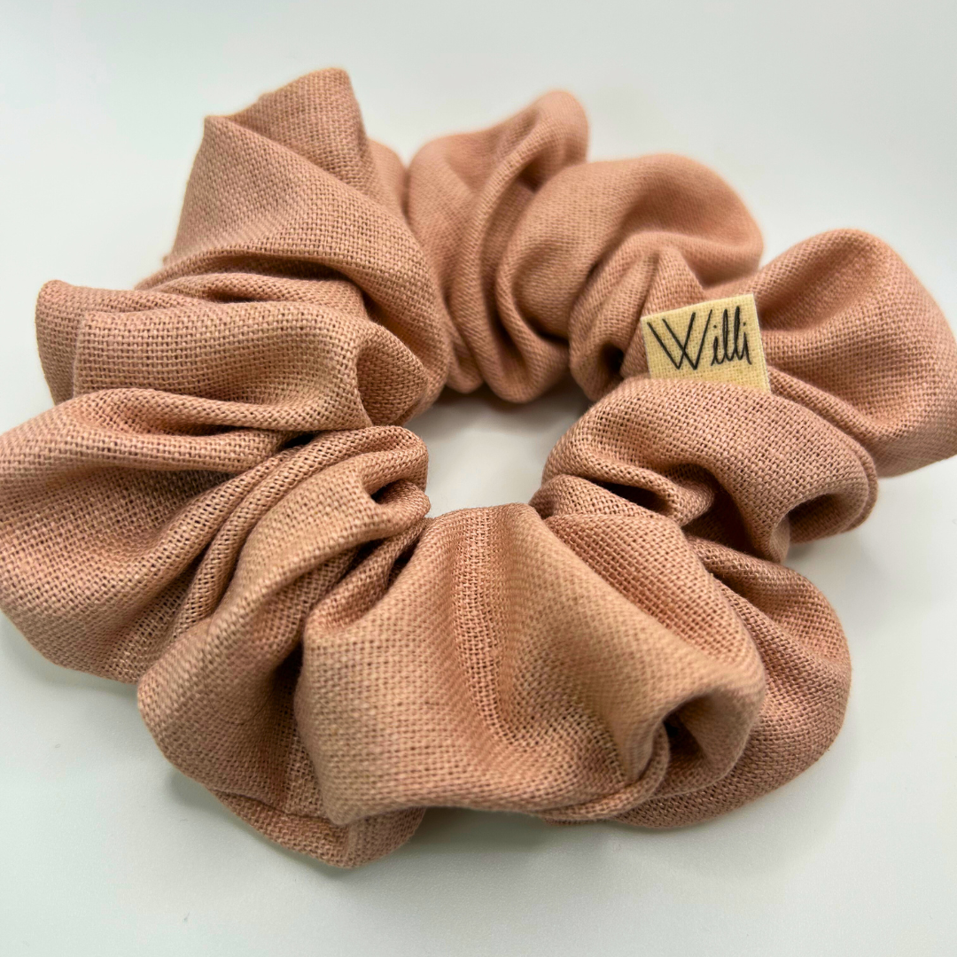 Pink scrunchie with a brand label on a light gray background