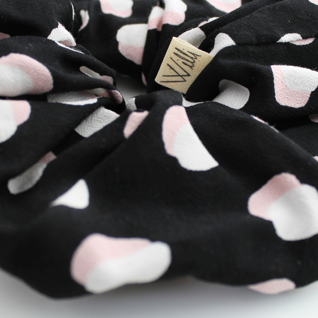 Black scrunchie with pink paw prints and a visible brand tag on a white background