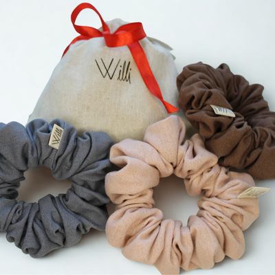 Set of three scrunchies in gray, beige, and brown with a branded pouch on a white background.