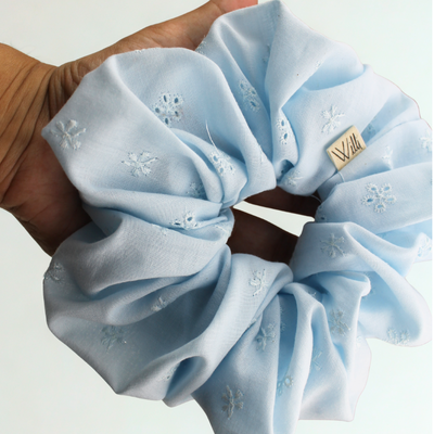 Light blue scrunchie with floral patterns held by a hand on a white background