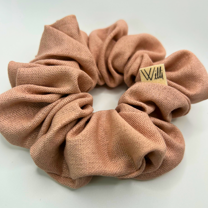 Pink scrunchie with a brand label on a light gray background