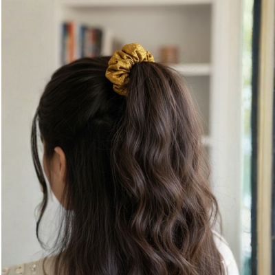 Person with wavy hair tied back with a gold scrunchie, indoor setting