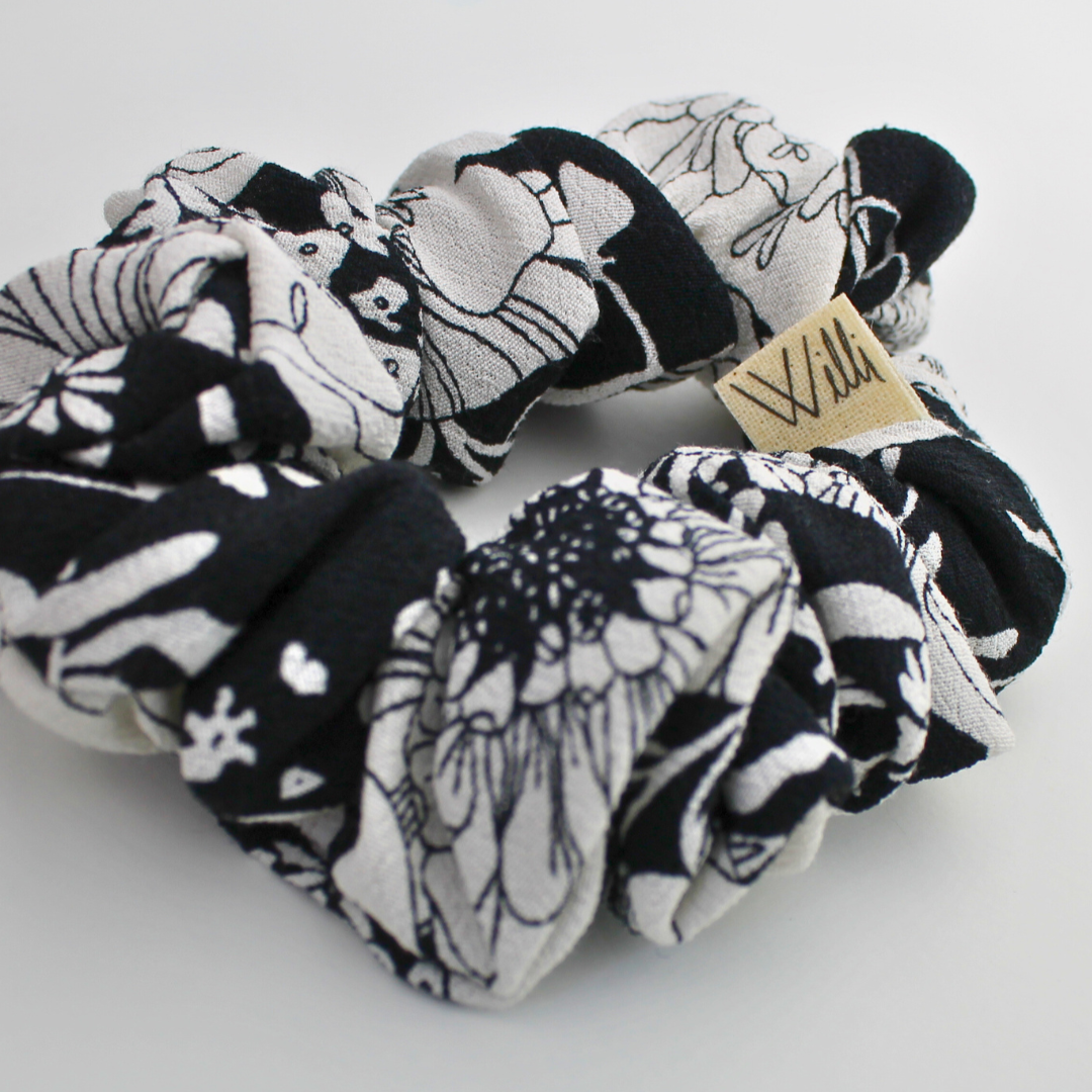 Set of black and white patterned scrunchies with a visible brand label on a light gray background