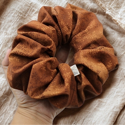 Brown textured scrunchie held by a hand on a beige fabric background