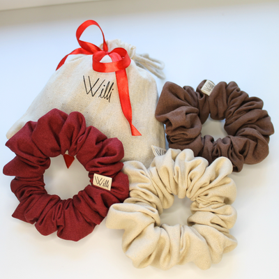 Three scrunchies in red, beige, and brown with a branded pouch on a white background