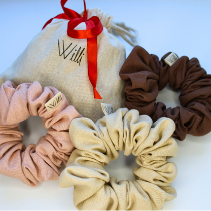 Set of three scrunchies in beige, pink, and brown with a branded pouch on a white background.