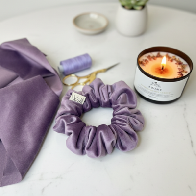 Purple scrunchie on a white surface with a candle and fabric in the background