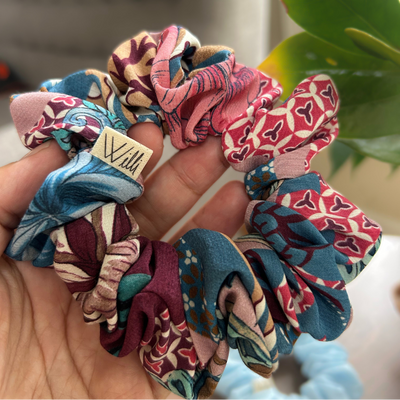 Hand holding colorful patterned scrunchies with a visible brand tag.