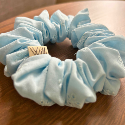 Light blue scrunchie with a brand tag on a wooden surface