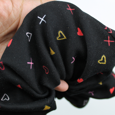 Black fabric with colorful heart patterns held by a hand on a white background