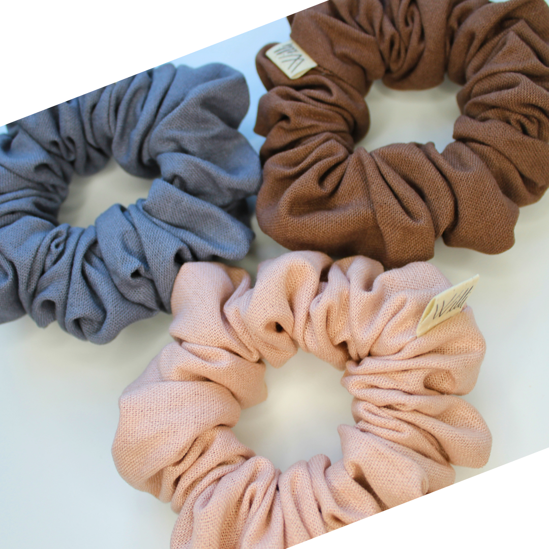 Three scrunchies in grey, brown, and pink on a white background