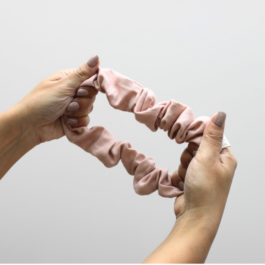 Pink scrunchies held by hands against a light gray background