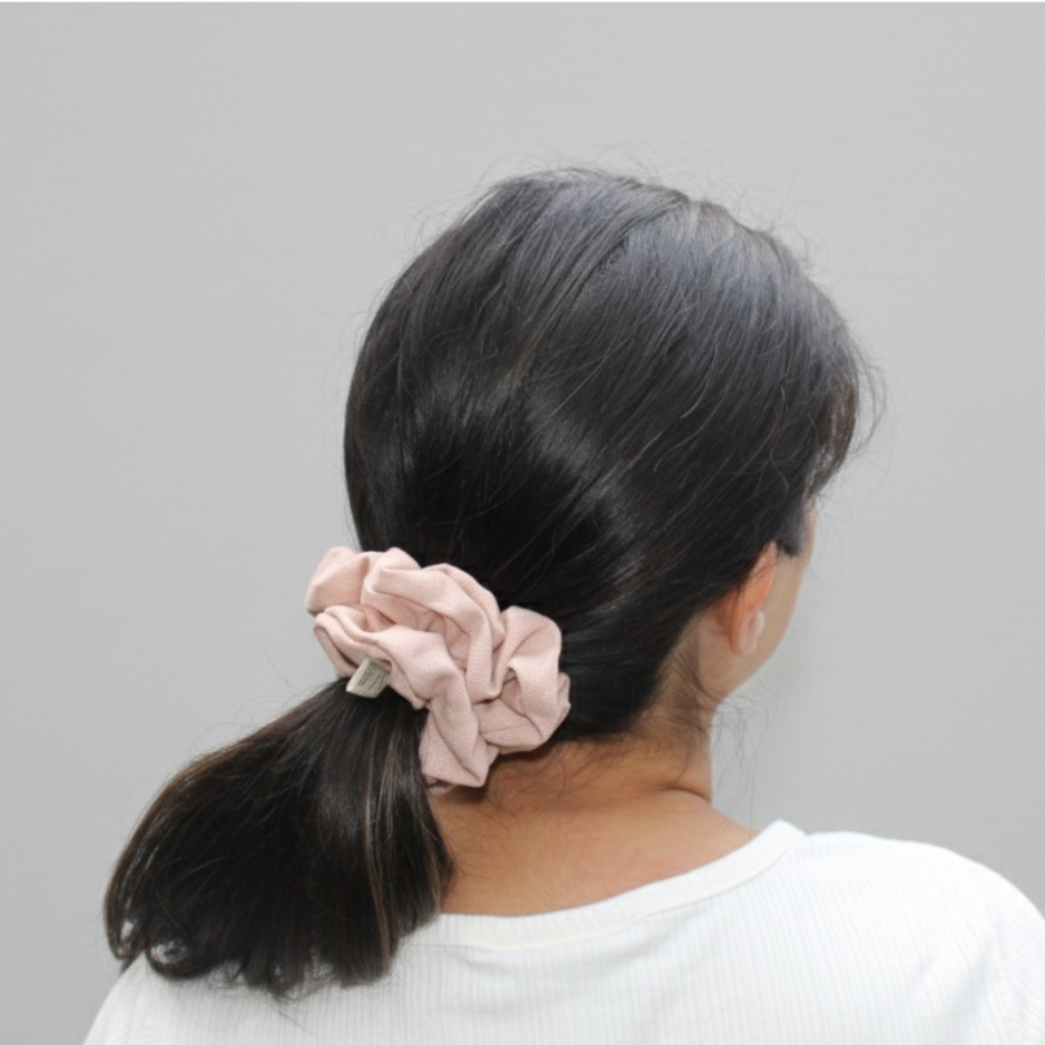 Person with a pink scrunchie in their hair against a gray background