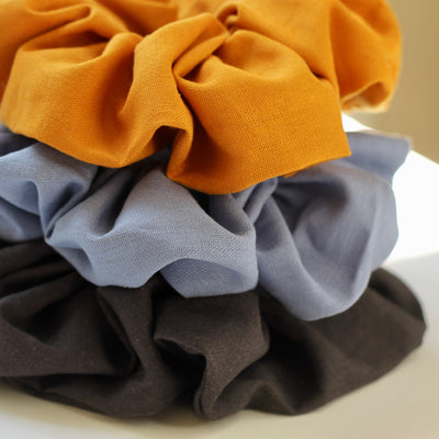 Three scrunchies in orange, blue, and dark grey on a beige background