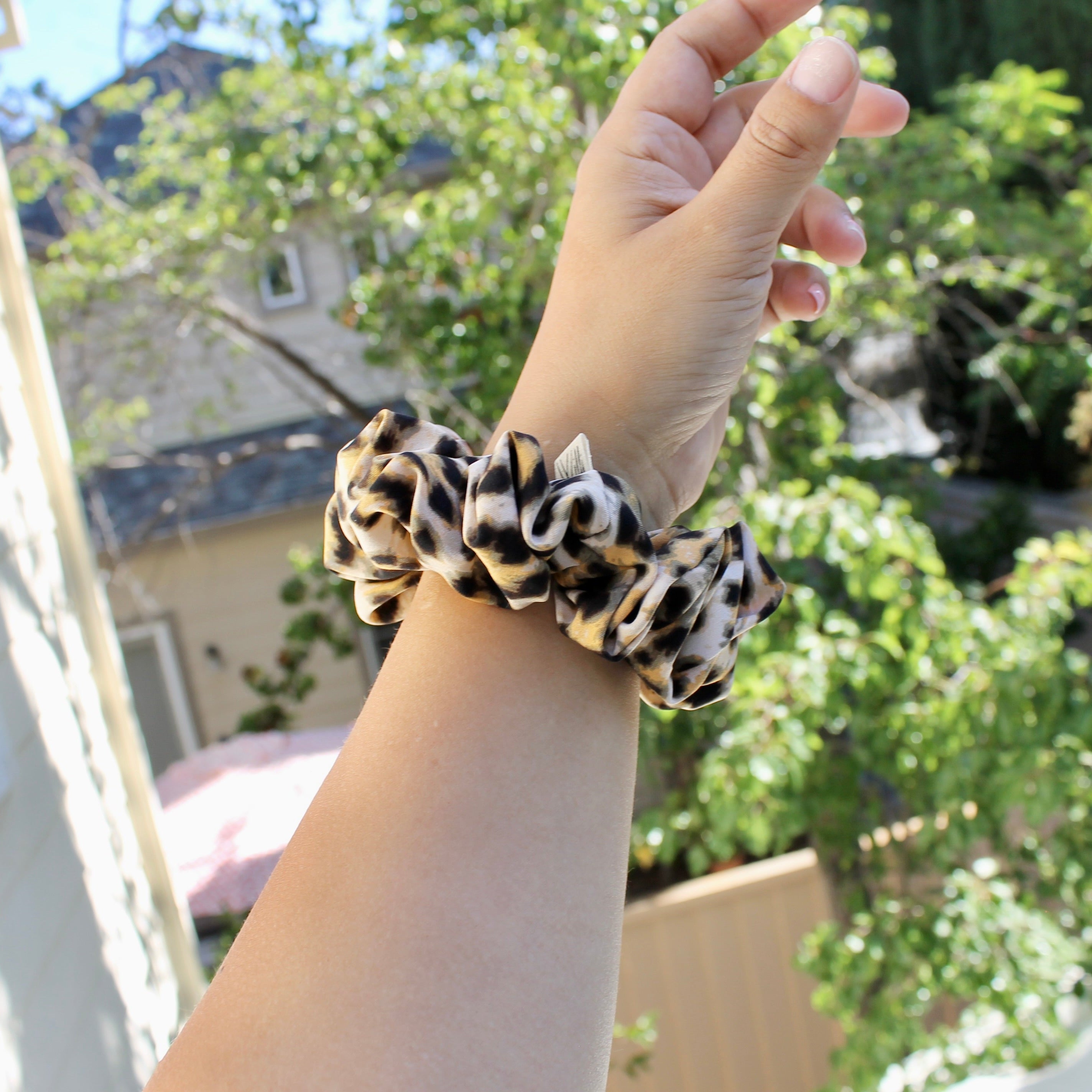 Hand wearing a leopard print scrunchie with a blurred outdoor background