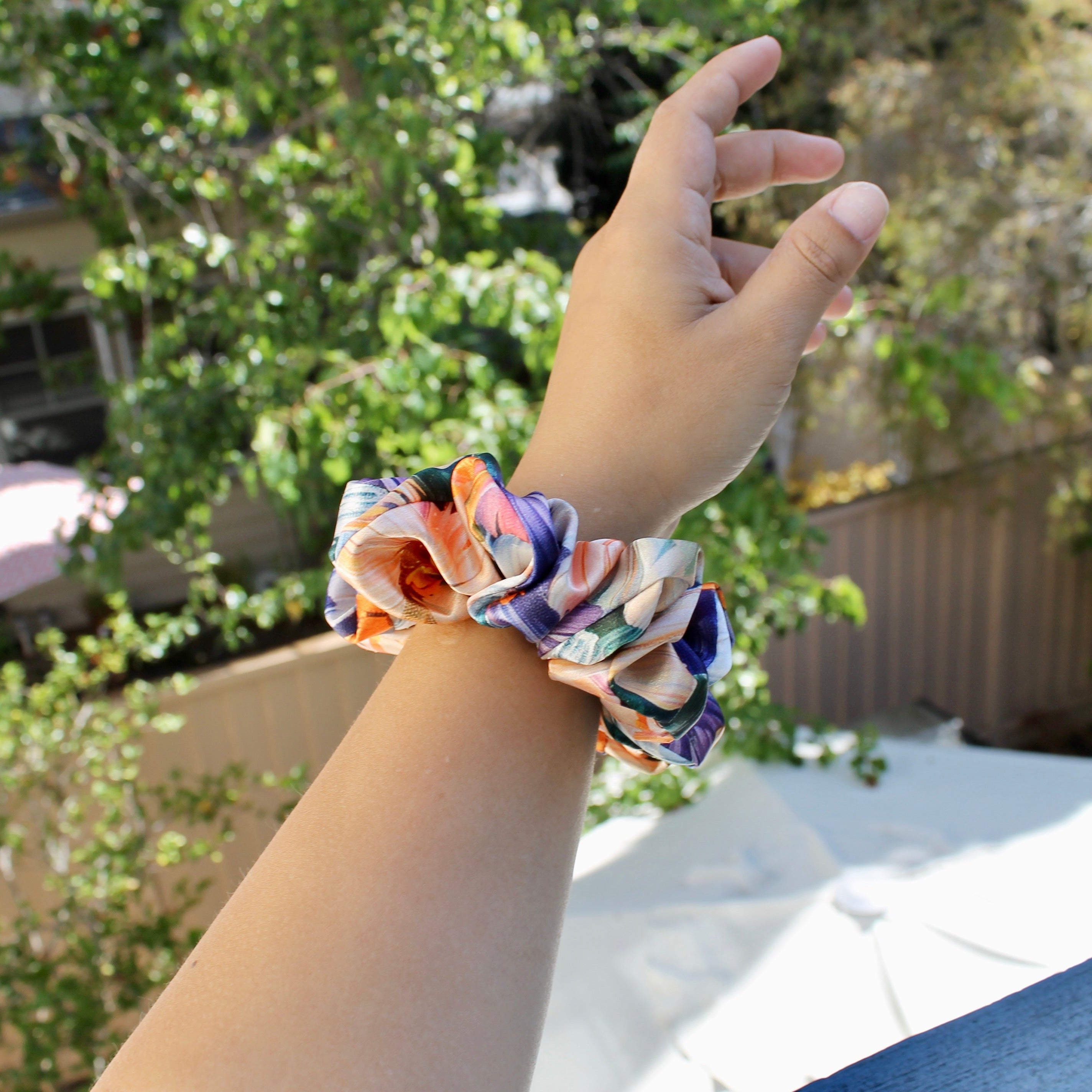Hand wearing a colorful scrunchie with a blurred outdoor background