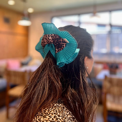 Person with teal hair bow and leopard print top in a blurred indoor setting