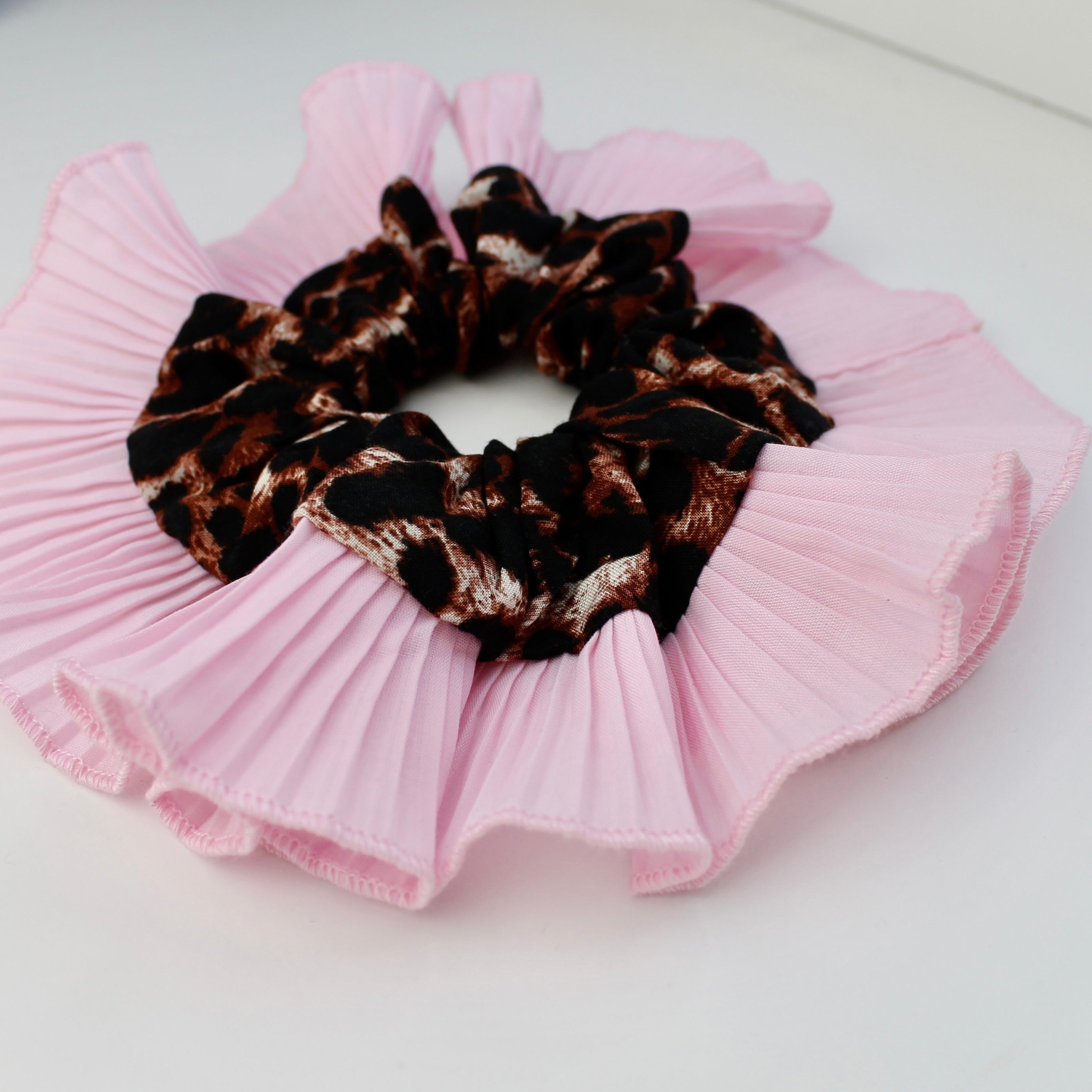 Leopard print scrunchie on a pink pleated fabric background