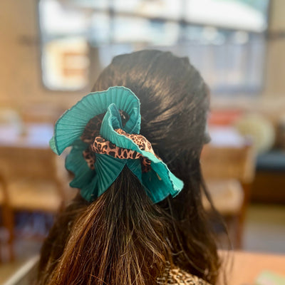 Person with teal hair accessory in a blurred indoor setting