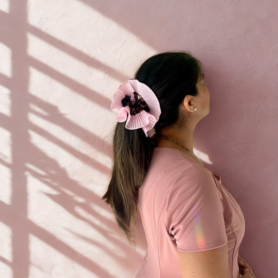 Person wearing a pink hair scrunchie against a pink wall with sunlight casting shadows.