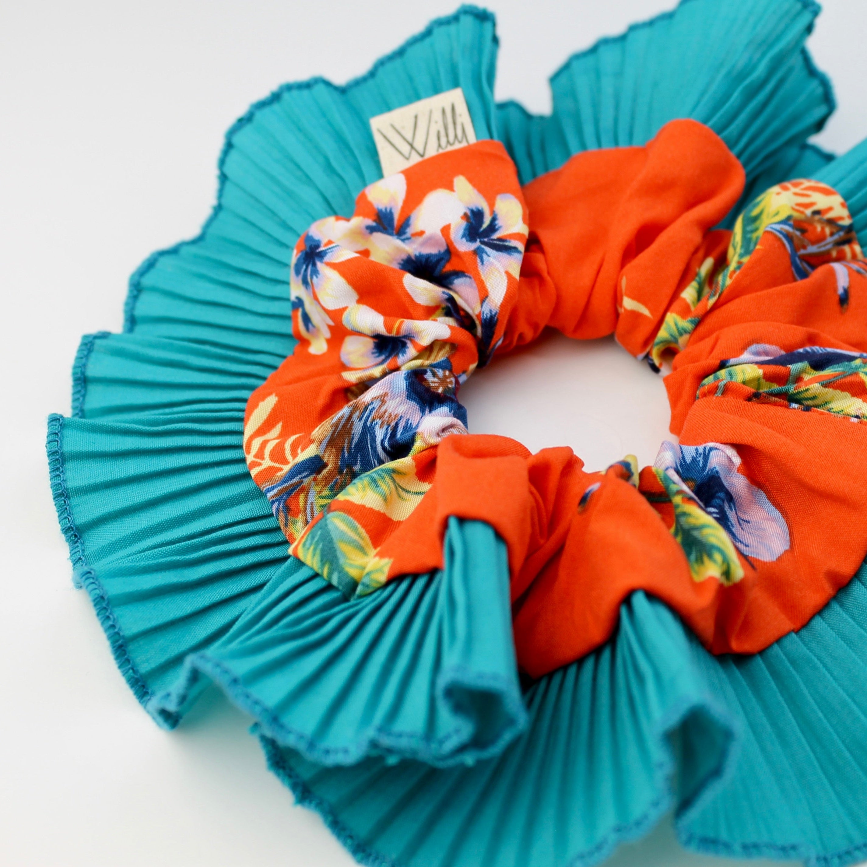 Turquoise scrunchie with floral patterned orange center on a white background