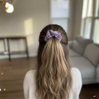 Person with long hair tied back with a purple scrunchie in a room with a couch and table.